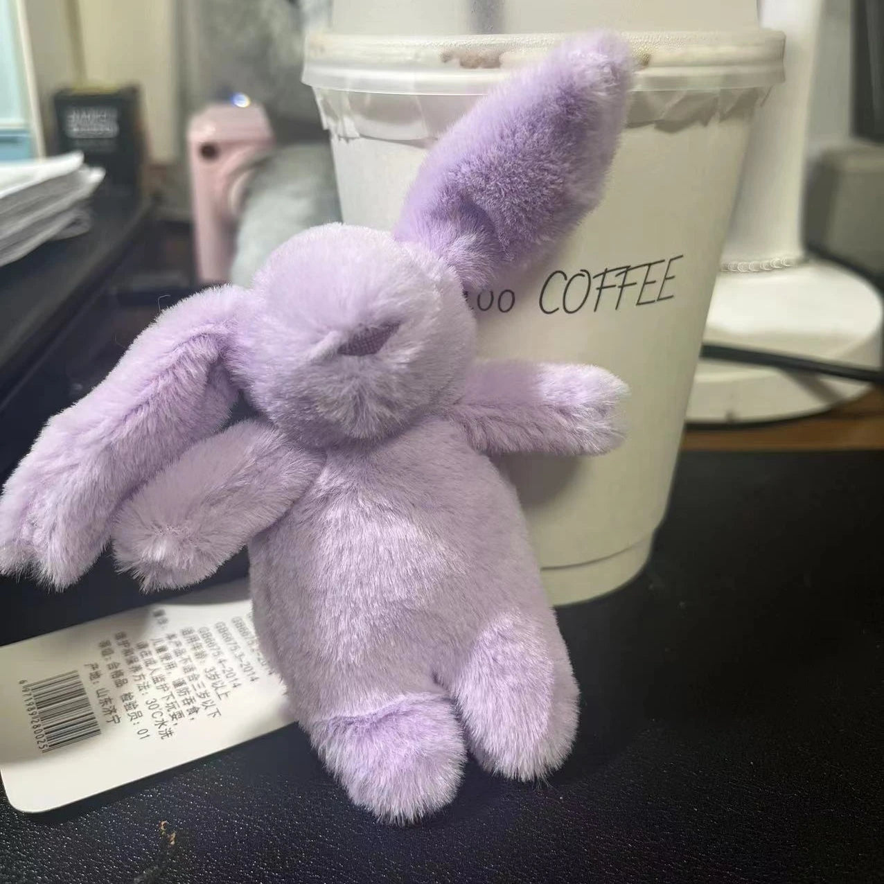 Llavero conejito morado sobre escritorio frente a un vaso de café desechable