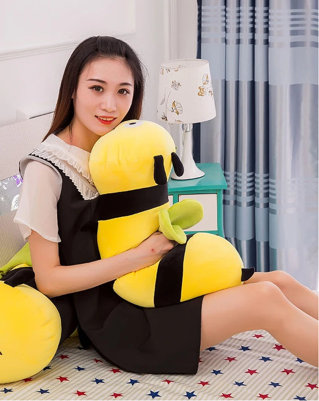 Modelo sentada en el suelo sosteniendo un peluche de abeja largo sobre su regazo, mostrando su flexibilidad