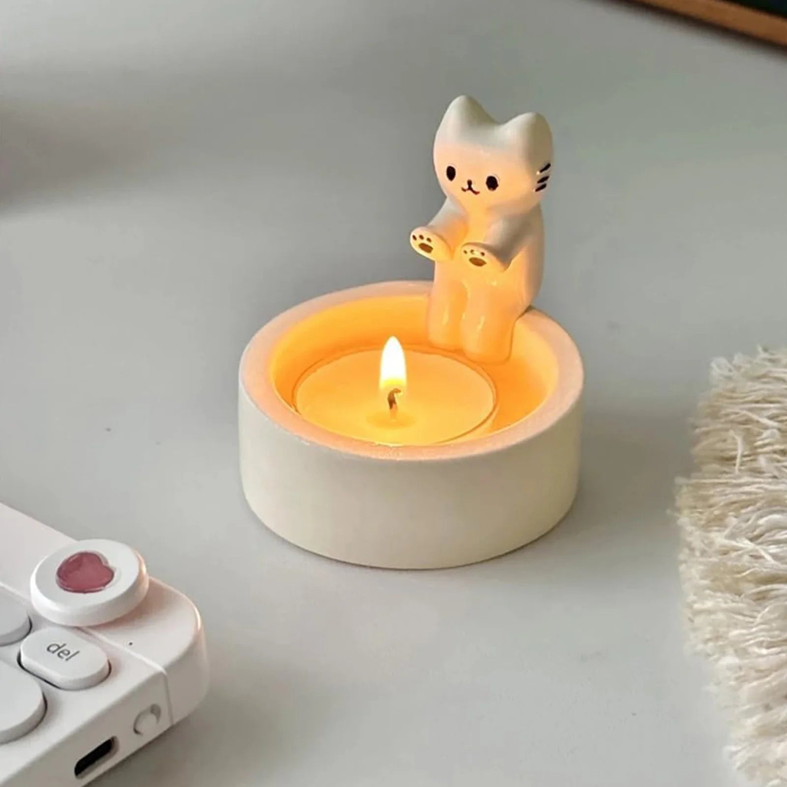 Portavela con gato blanco con vela tea light encendida sobre un escritorio blanco, con parte de un portátil visible