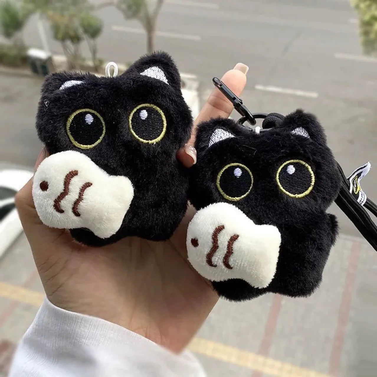 Dos llaveros kawaii de gatito negro con pez blanco sostenidos en la mano