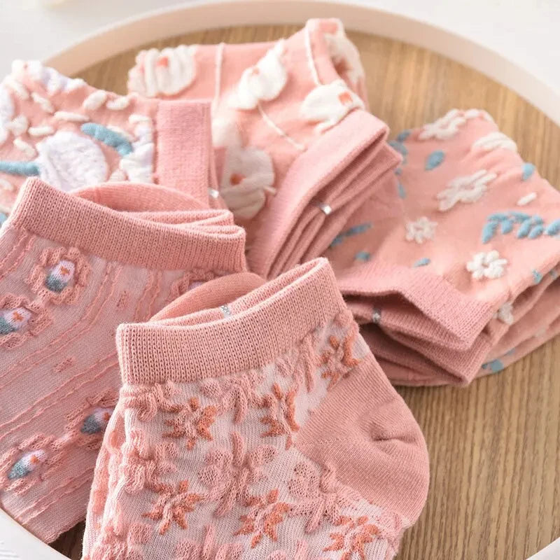 Cinco pares de calcetines con flores doblados sobre una superficie de madera, superpuestos, con el par frontal en foco y los del fondo ligeramente desenfocados