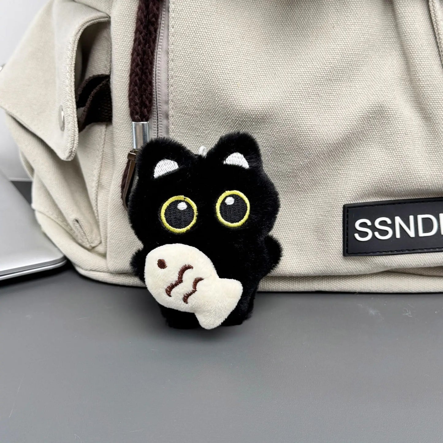 Llavero de gatito negro con pez blanco colgado en una mochila