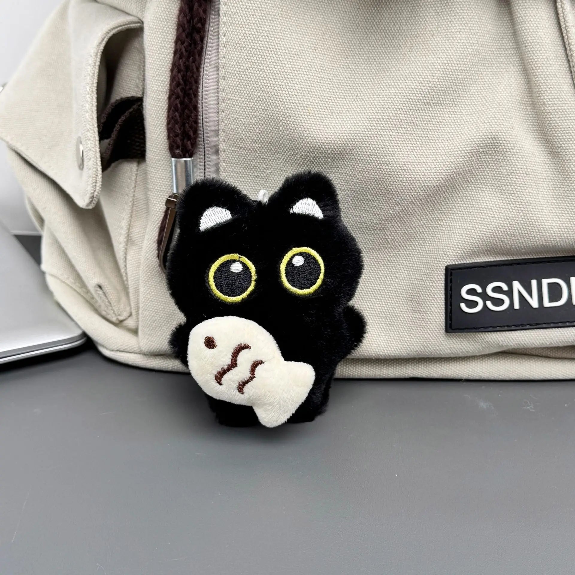 Llavero de gatito negro con pez blanco colgado en una mochila